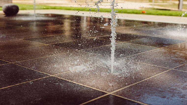 Een waterstraal spuit uit de grond op een gladde plek. De omgeving lijkt helder en uitnodigend.