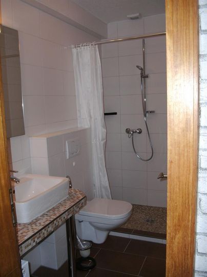 Ein modernes Badezimmer mit einer Dusche, einem Waschbecken und einer Toilette. Die Wände sind hell gefliest, und das Design ist schlicht und funktional.