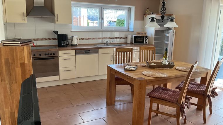 A modern kitchen with a wooden dining table and chairs. There are windows that let in plenty of natural light.