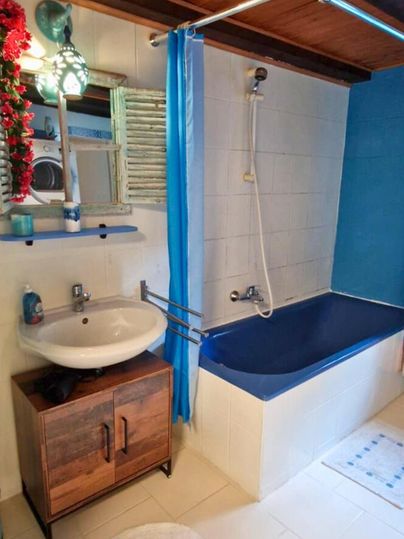 A bathroom with a bathtub, a sink, and a blue wall. The wooden ceiling gives the room a cozy atmosphere.