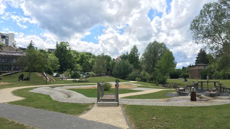 A beautiful park with lush greenery and winding paths. The clouds in the sky create a relaxed atmosphere.
