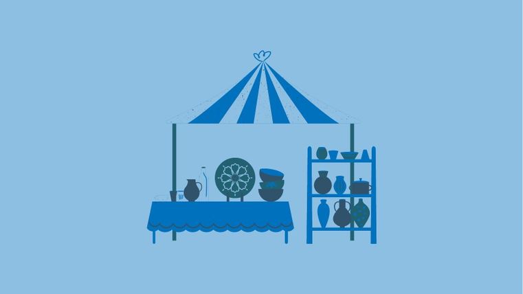 A market stand with a blue tent and various pots and dishes. The stand has a tablecloth and shelves with additional ceramics.