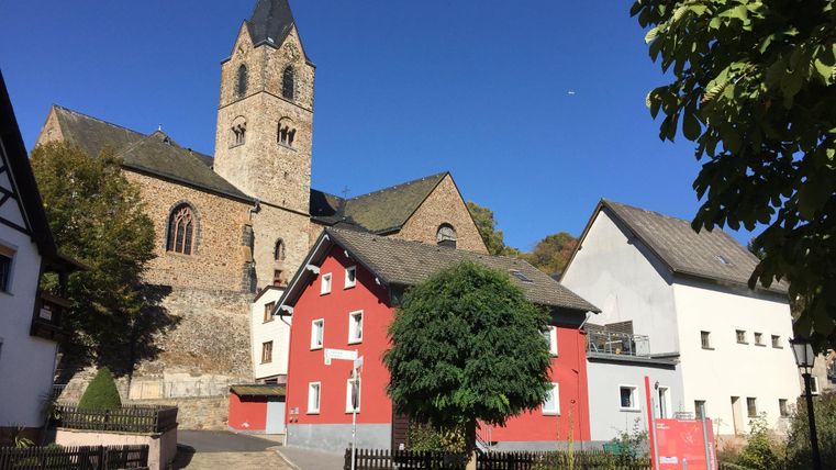 A picturesque street with old houses and an impressive church in the background. The sky is clear and blue, making the scene cheerful.