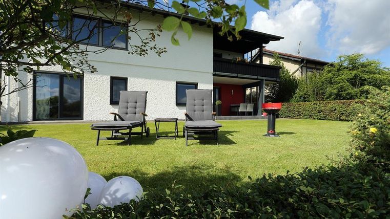 Een verzorgde tuin met twee ligstoelen en een barbecue. Het gebouw op de achtergrond heeft grote ramen en geeft een uitnodigende indruk.