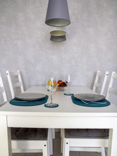 A bright dining area with a white table and chairs. Above the table hang decorative lamps and the table is lovingly set with dishes.