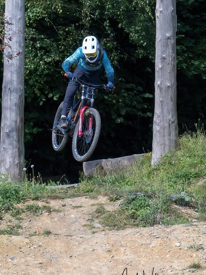 Een fietser springt over een sprongetje in het bos. De rijder draagt een helm en strakke kleding.