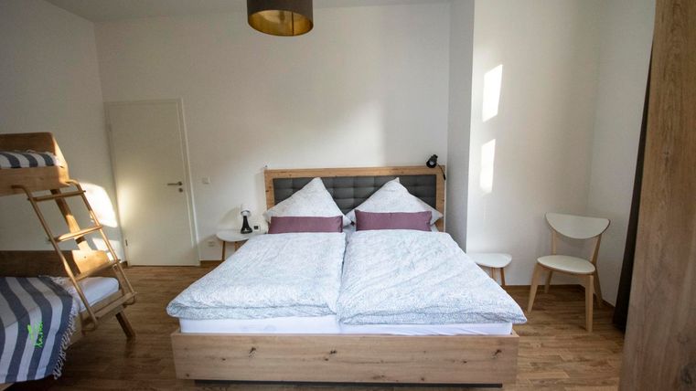 Ein gemütliches Schlafzimmer mit einem großen Doppelbett und Holzfußboden. Es gibt einen Stuhl, eine Treppe zu einem Hochbett und viel natürliches Licht.