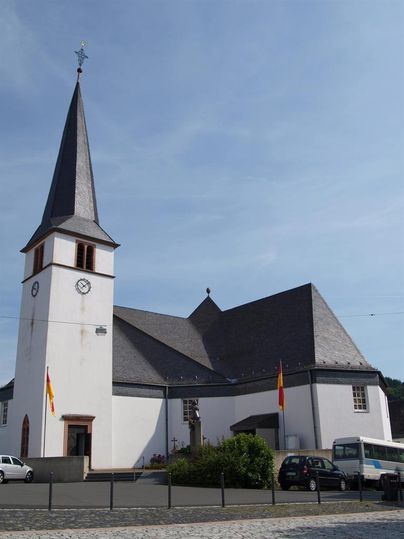 Eine schöne Kirche mit einem hohen, spitzen Turm und einem weißen Gebäude. Das Wetter ist klar und sonnig.