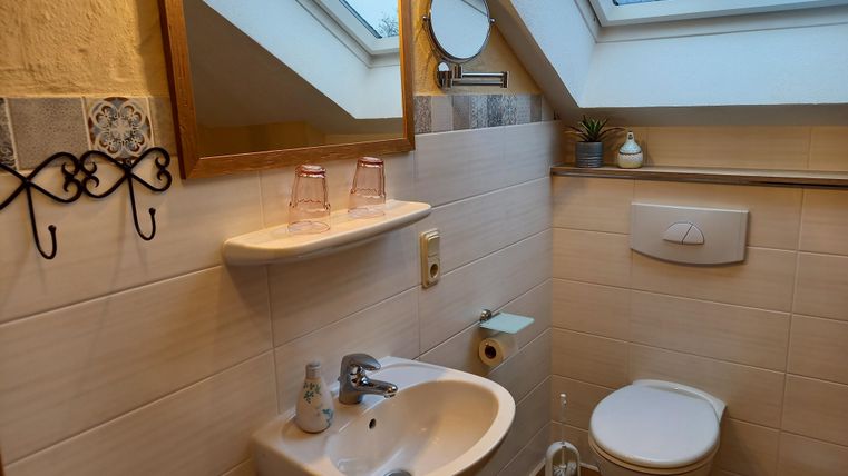 Een kleine badkamer met een wastafel, een toilet en een groot raam. De ruimte is licht en modern ingericht.