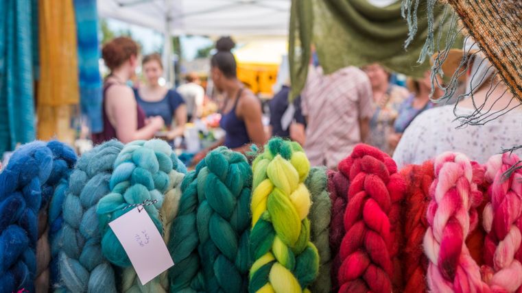 A colorful market stall with various colored yarn strands. In the background, people can be seen looking around and shopping.