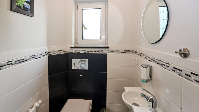 Een moderne badkamer met een toilet en een kleine wastafel. Een raam en een ronde spiegel zorgen voor natuurlijk licht en een heldere sfeer.