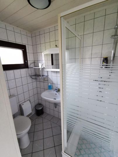 Een moderne badkamer met een douche, een wastafel en een toilet. De muren zijn betegeld met witte tegels en er is een raam voor natuurlijk licht.