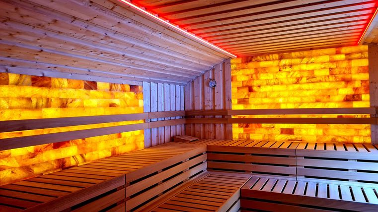Ein modernes Sauna-Interior mit Holzliegen und sanfter Beleuchtung. Die Wände sind mit farbigen Salzkristallen gestaltet.