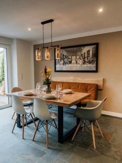 Ein modern eingerichteter Essbereich mit einem Holztisch und eleganten Stühlen. An der Wand hängt ein großes Bild, und eine schöne Blumenvase steht auf dem Tisch.