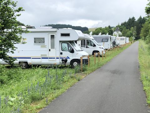 Several motorhomes line a path, surrounded by lush greenery. The atmosphere is calm and idyllic.