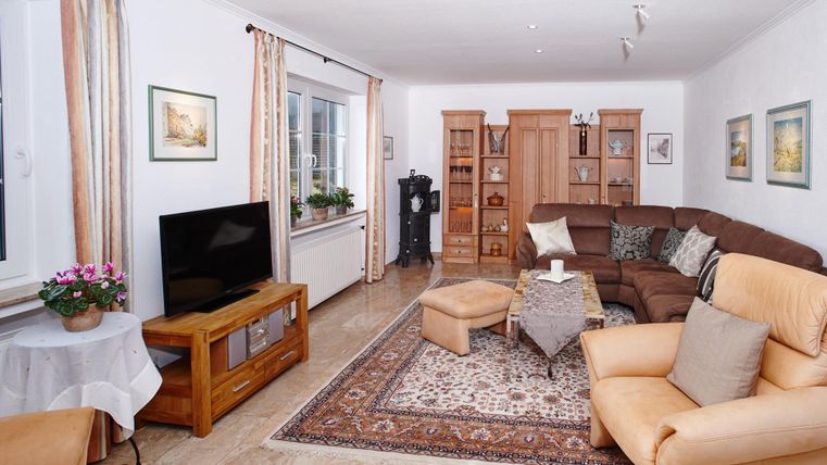 Ein gemütliches Wohnzimmer mit einer großen Couch und einem Fernseher. Helle Wände und Holzregale schaffen eine einladende Atmosphäre.