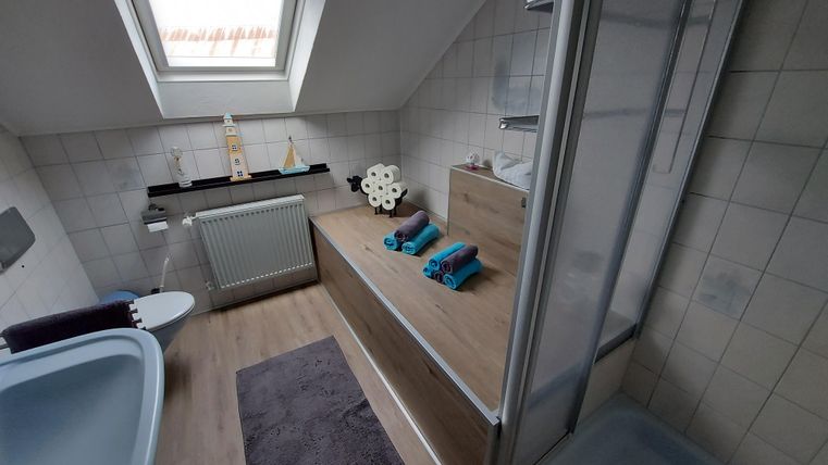 A modern bathroom with a window and wooden shelves. The clean design includes a bathtub, a shower, and decorative towels.