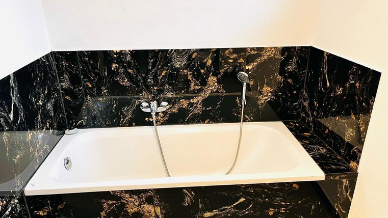 An elegant bathtub made of white acrylic sits on a stylish black marble base. The room has a modern and luxurious atmosphere.