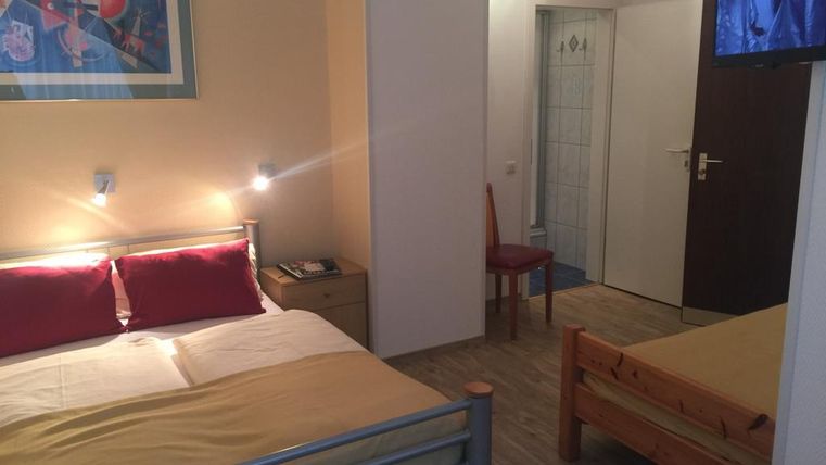 Ein einfaches Zimmer mit zwei Betten, einem Fernseher und einem kleinen Tisch. Die Wände sind hell und es gibt ein Kunstwerk über dem Bett.