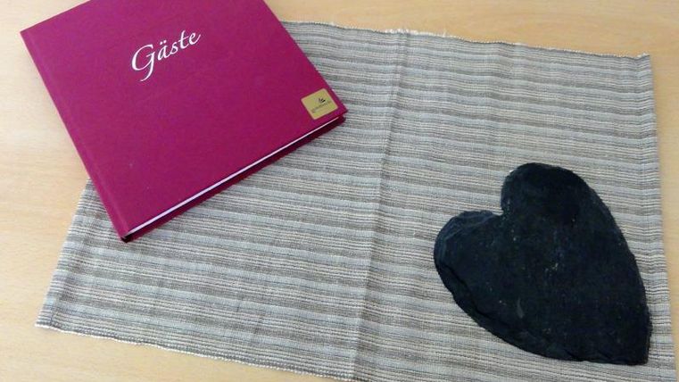 A red guestbook lies on a striped cloth. Next to the book is a black stone heart.