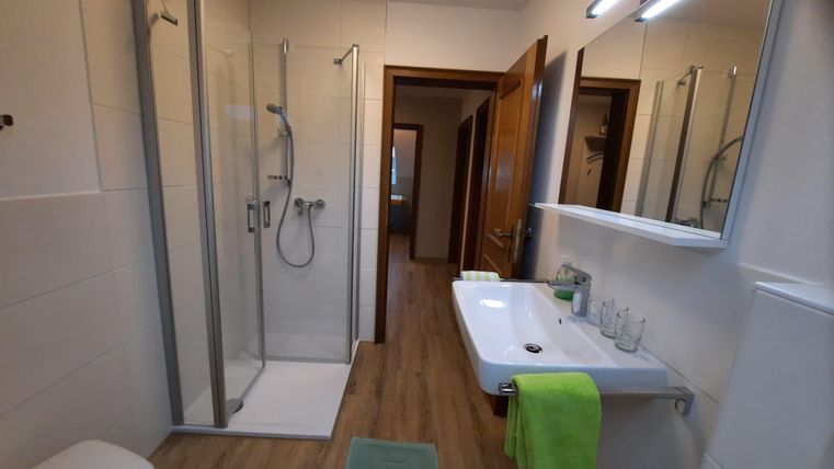 A modern bathroom with a shower and a sink. The walls are brightly tiled and there are wooden details in the floor.