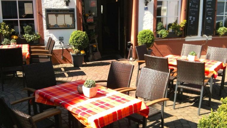 Een gezellige buitenruimte van een restaurant met rustieke tafels en stoelen. De tafels zijn versierd met een rood-geruite tafelkleed en omringd door kleine planten.