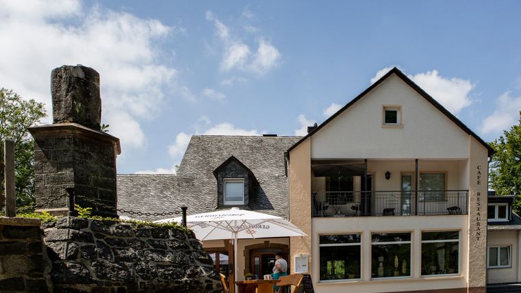 Ein modernes Gebäude mit einer hellen Fassade und großen Fenstern. Im Vordergrund befindet sich eine gemütliche Terrasse mit Sitzmöglichkeiten.