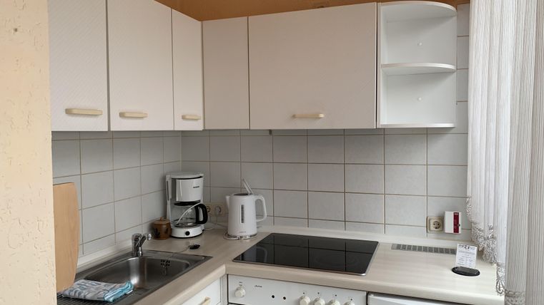 Eine moderne Küche mit weißen Schränken und hellen Wänden. Sie ist mit einem Herd, einer Mikrowelle und einer Kaffeemaschine ausgestattet.