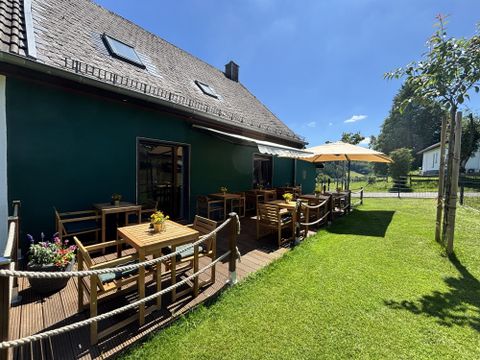 Terras van het café met meerdere tafels en stoelen naast een groene weide.