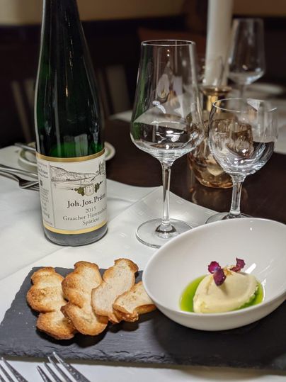 Ein elegantes Tischarrangement mit einem Wein, Gläsern und einer Vorspeise. Die Vorspeise besteht aus knusprigem Brot und einem cremigen Dip auf einem schwarzen Steinplatte.