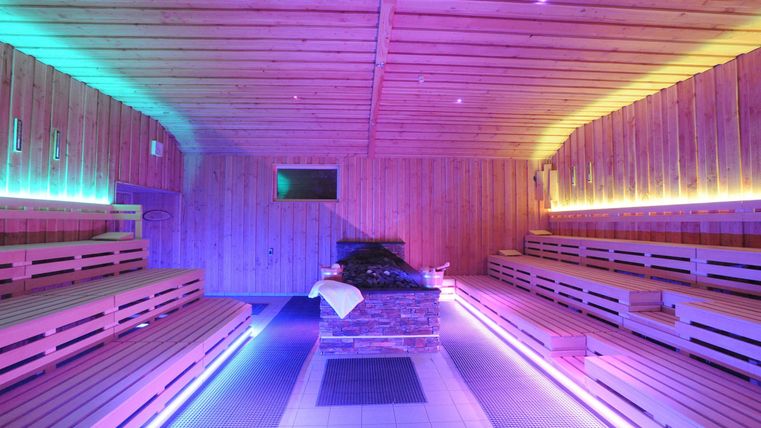 Eine moderne Sauna mit Holzbank und bunten LED-Lichtern. Der Raum strahlt eine entspannende Atmosphäre aus.