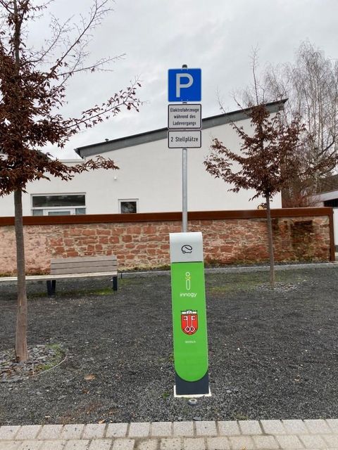 Een parkeerplaats met een parkeerautomaat in een rustige woonwijk. Op de achtergrond zijn bomen en een modern gebouw te zien.