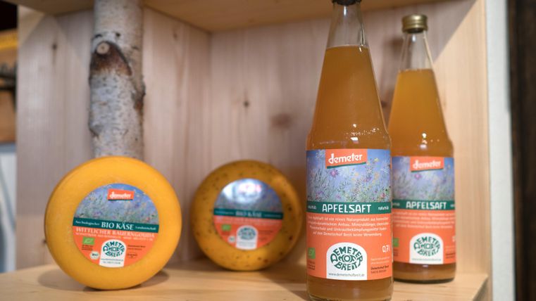 Eine Auswahl an Demeter-Produkten, darunter Käse und Apfelsaft. Die Verpackungen sind bunt und informativ gestaltet.