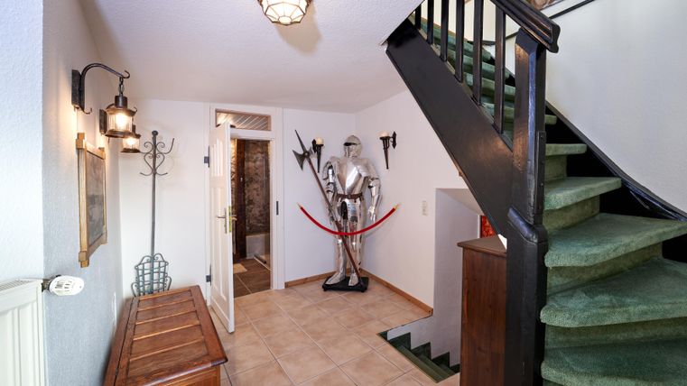 An entrance with a staircase and a wooden cabinet. In the center is an armor, surrounded by antique furniture and a cozy atmosphere.