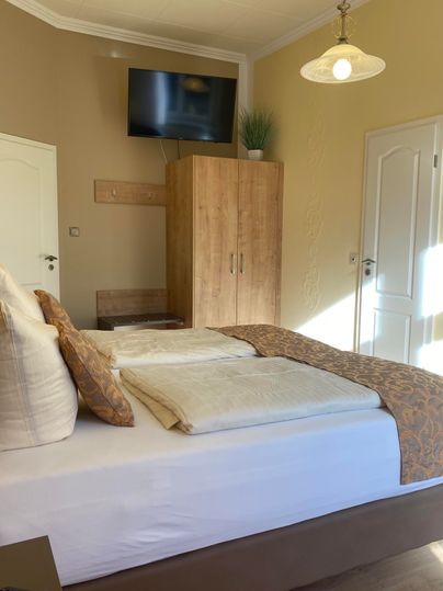 Ein gemütliches Zimmer mit einem Doppelbett und modernen Möbeln. An der Wand hängt ein Fernseher und es gibt einen Schrank aus Holz.