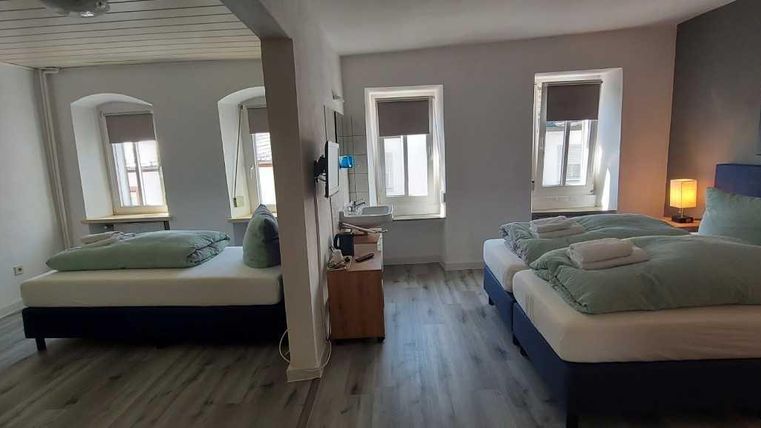 Ein modernes Hotelzimmer mit zwei Betten und Fenstern, die viel Tageslicht hereinlassen. Die Wände sind in hellen Farben gestrichen, und die Einrichtung ist schlicht und elegant.