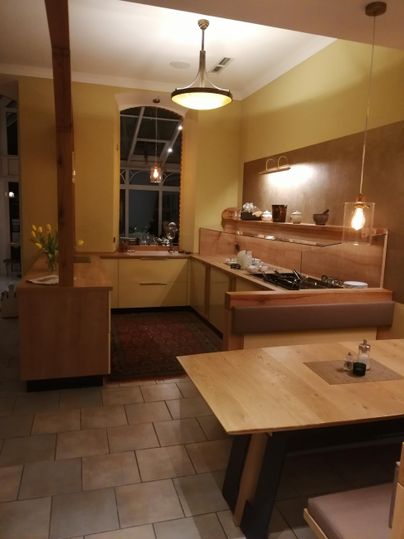 Eine moderne Küche mit Holzschränken und einem großen Esstisch. Die Wände sind gelb gestrichen und es gibt eine warme Beleuchtung.