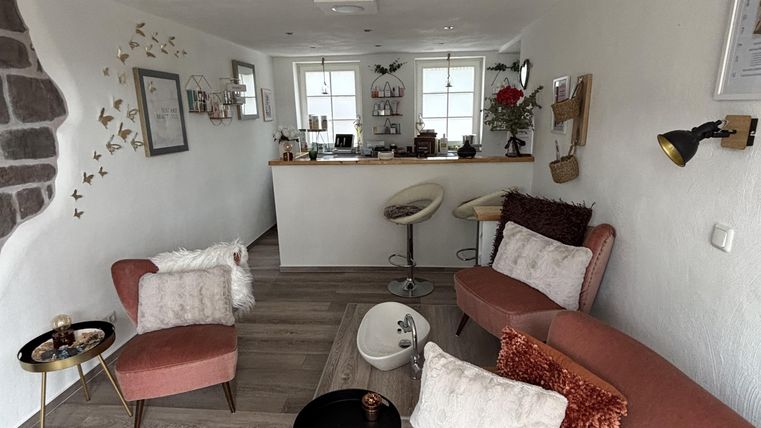 Een moderne ontvangst- en wellnessruimte met roze meubels en stijlvolle accenten. Er is een ronde tafel en decoratieve elementen aan de muren.