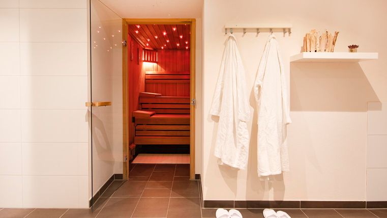 A modern sauna area with an inviting entrance. Two bathrobes and flip-flops hang on the wall.