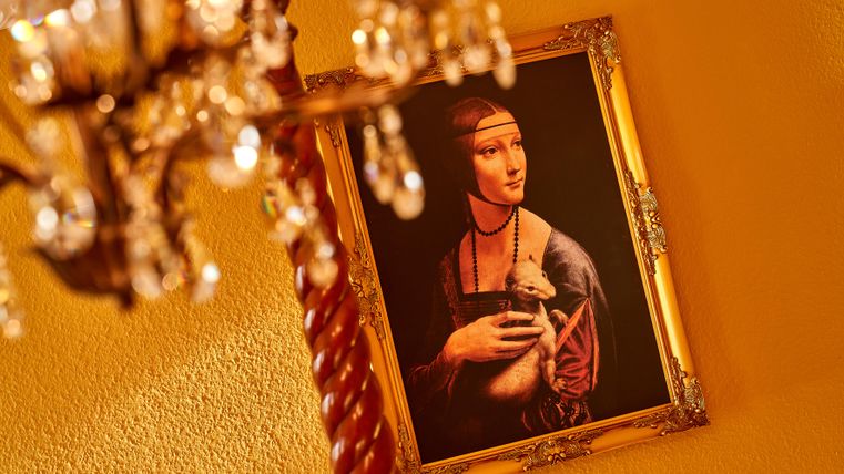 An artistic painting of a woman with a child in her arms, hanging on a yellow wall. In the foreground, a beautiful chandelier is visible.