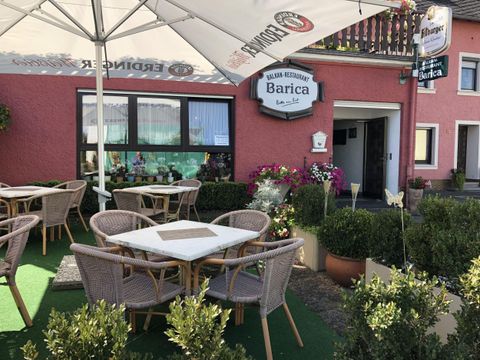 Ein gemütliches italienisches Restaurant mit Außenbereich und Tischen. Blühende Pflanzen und Sonnenschirme schaffen eine einladende Atmosphäre.
