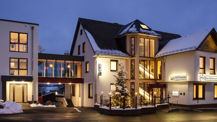 Ein modernes Hotelgebäude mit warmem Licht und Schneebedecktem Boden. Es ist Nacht und die Architektur ist einladend.