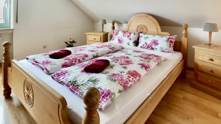 Ein gemütliches Schlafzimmer mit einem großen Holzbett und floralen Bettwäsche. Neben dem Bett stehen zwei Nachttische mit Lampen.