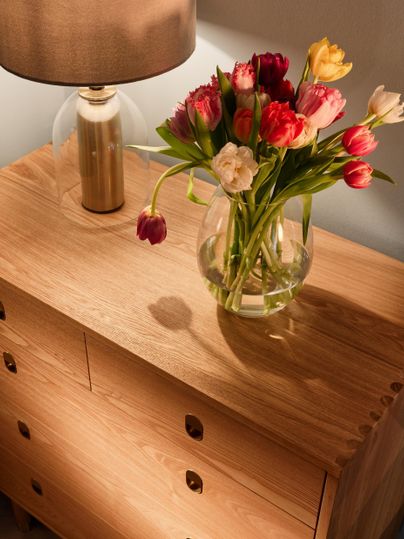 A wooden table with a modern lamp and a glass vase full of colorful tulips. The warm colors create a cozy atmosphere.