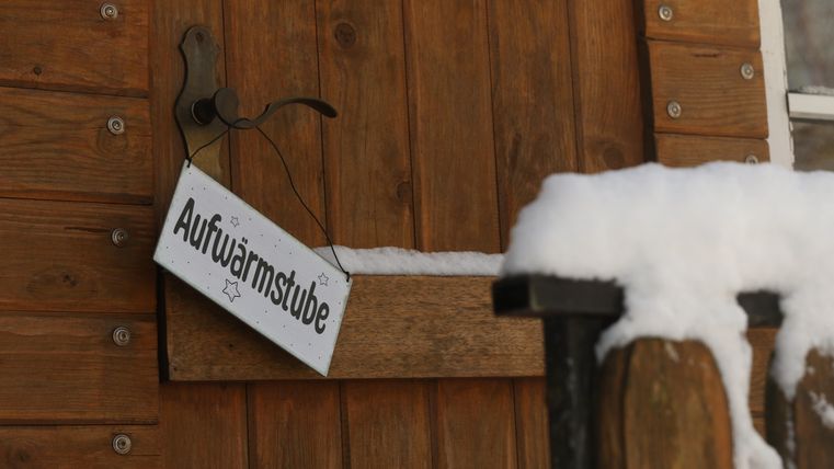 A wooden shed with a sign that says "Warm-up Room." Snow lies on the railing, creating a cozy winter atmosphere.
