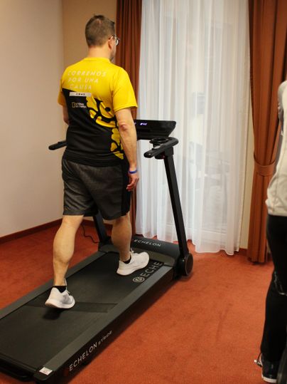 Ein Mann läuft auf einem Laufband in einem hellen Raum. Er trägt ein gelbes T-Shirt und kurze Sporthose.