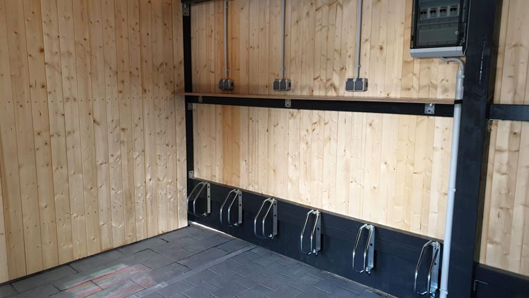 Ein leerer Raum mit Holzpanelen und mehreren Halterungen an der Wand. Der Boden ist aus schwarzen Fliesen.