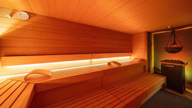 Een gezellige sauna met houten bank en zachte verlichting. Op de achtergrond staat een kachel voor de warmte.