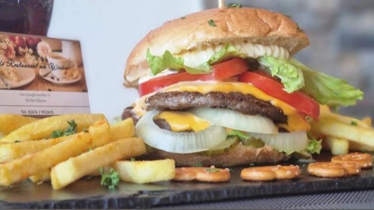 Ein saftiger Burger mit Käse, Salat, Tomate und Zwiebeln. Dazu knusprige Pommes frites und ein Getränk.