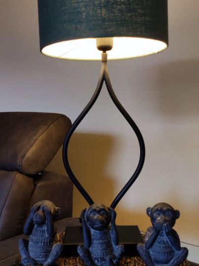 Eine Tischlampe mit einem blauen Lampenschirm steht auf einem Tisch. Darunter sitzen drei Dekorationsfiguren in Form von Affen.